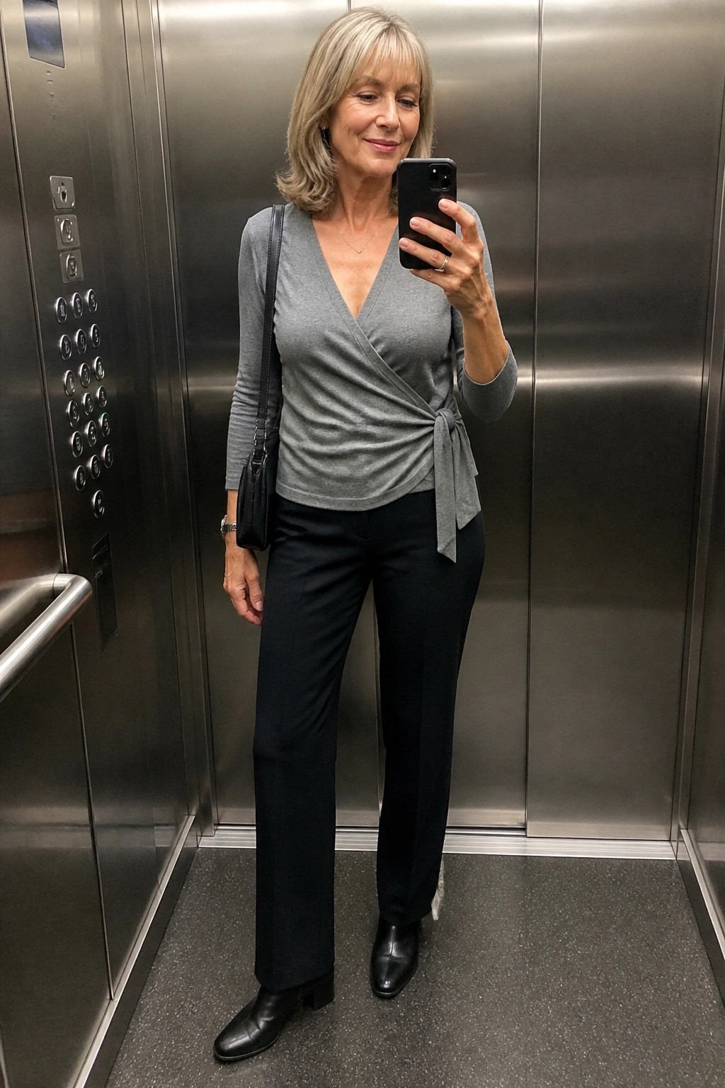 Woman in gray wrap top and black pants taking selfie in elevator