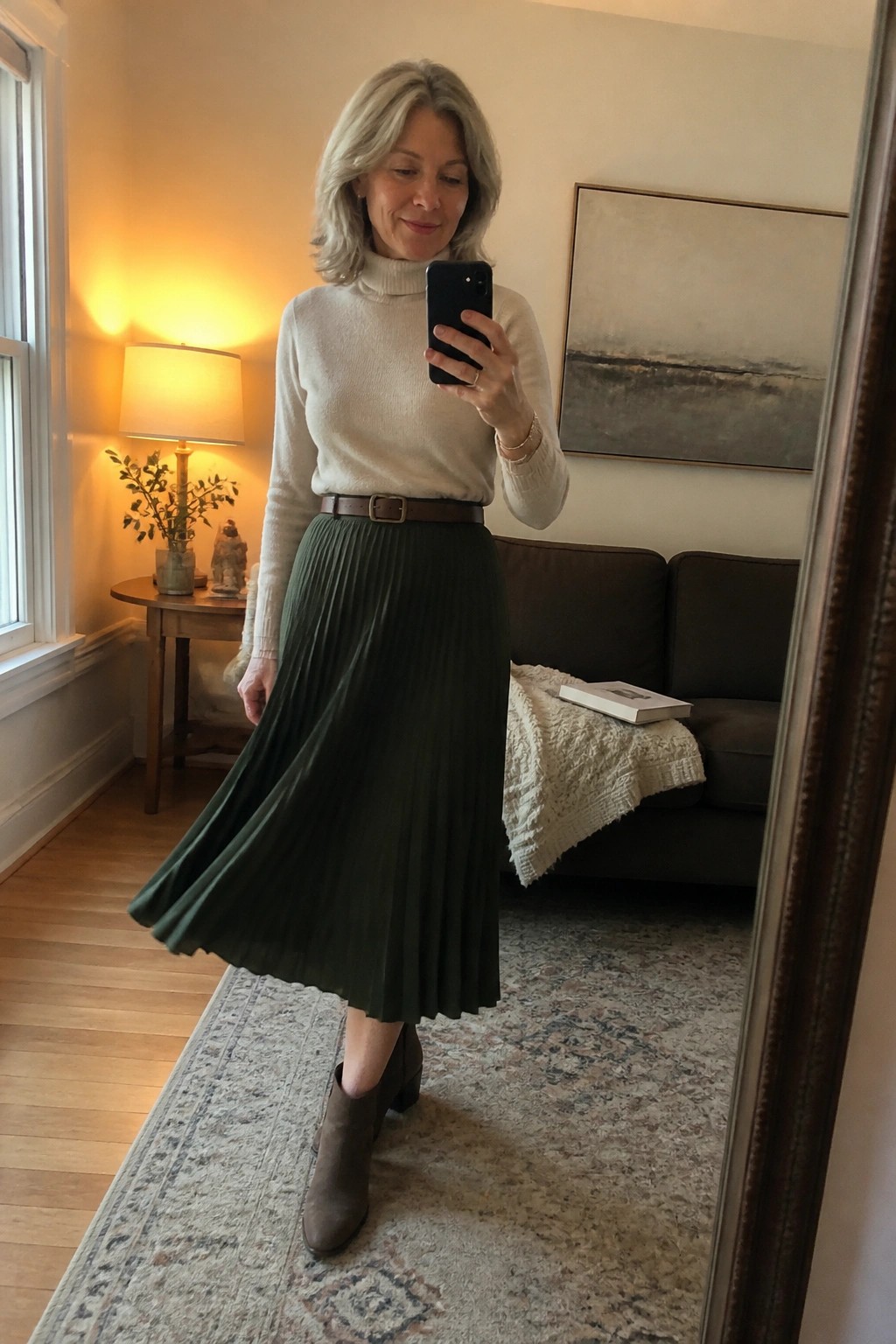 Silver-haired woman in white turtleneck and green pleated skirt taking mirror selfie