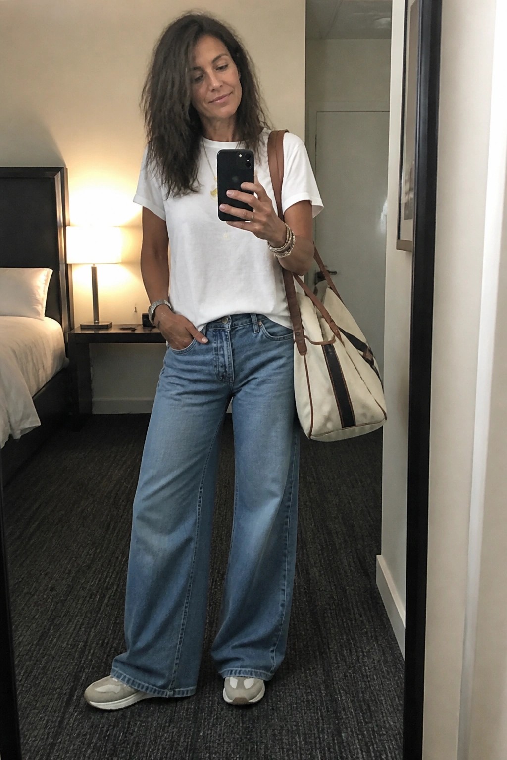 Woman in white tee and wide-leg jeans taking mirror selfie with tote bag