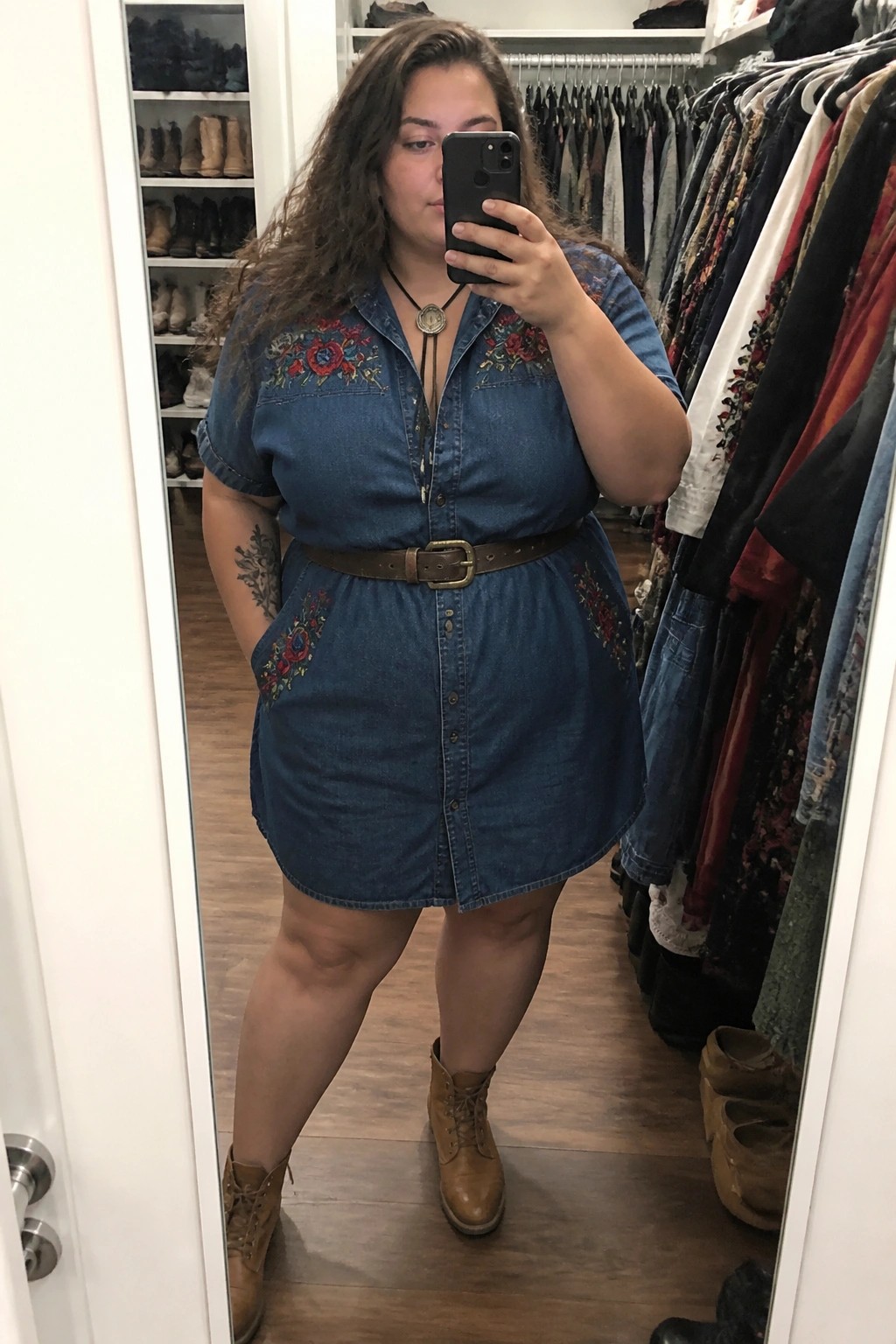 Woman in blue embroidered denim dress taking mirror selfie in closet