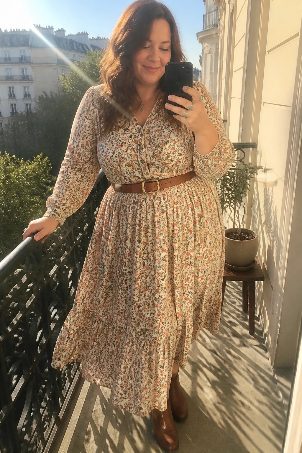 Woman in floral midi dress with brown belt taking balcony selfie