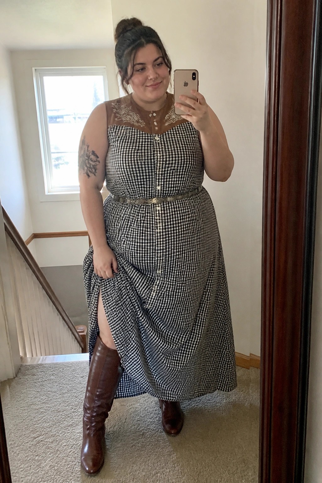Woman in black gingham dress and brown boots taking mirror selfie