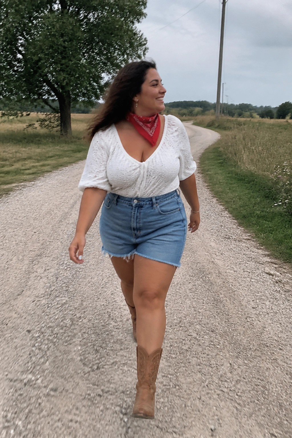 Woman in white lace top, denim shorts, and cowboy boots on rural gravel road