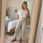 Blonde woman in white t-shirt and beige wide-leg linen pants taking mirror selfie.