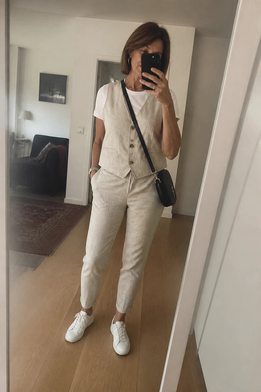 Woman in beige linen vest and pants taking mirror selfie with phone