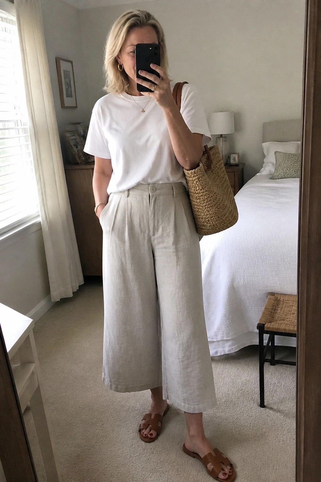 Blonde woman in white t-shirt and beige wide-leg linen pants taking mirror selfie.
