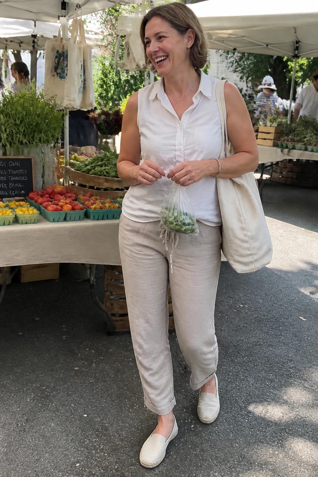 Woman in white shirt and beige pants holding greens at farmers market