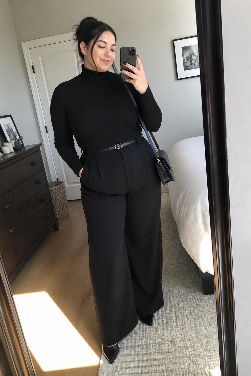 Woman taking mirror selfie in black turtleneck and wide-leg pants in bedroom