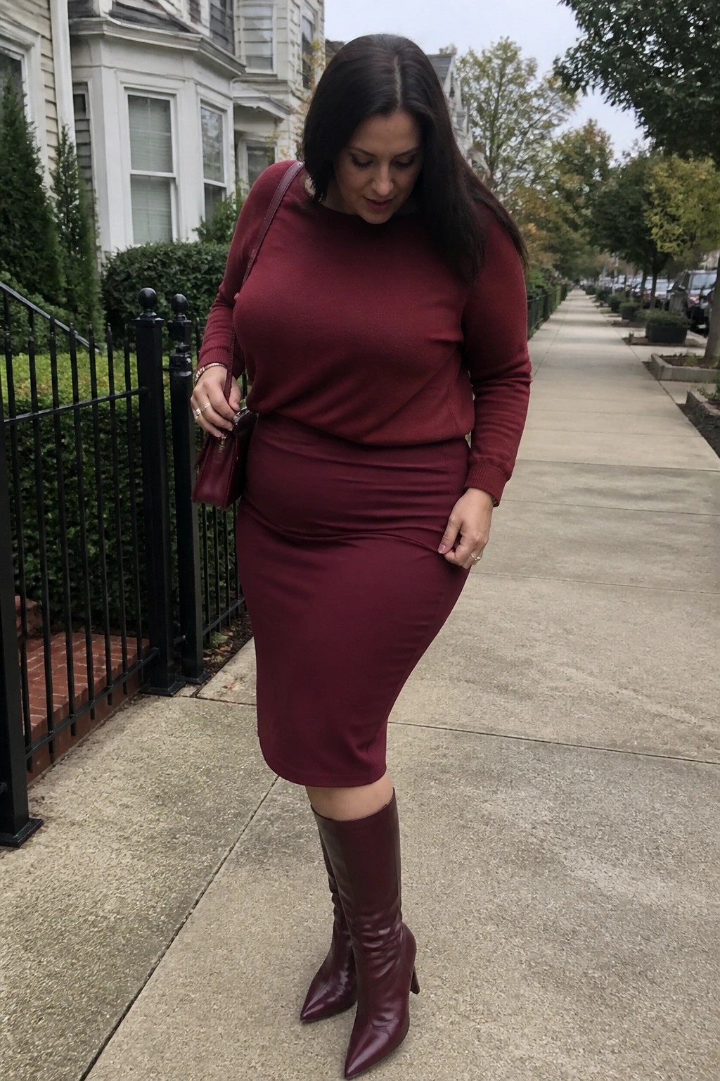 Woman in matching maroon sweater, skirt, and knee-high boots on suburban sidewalk