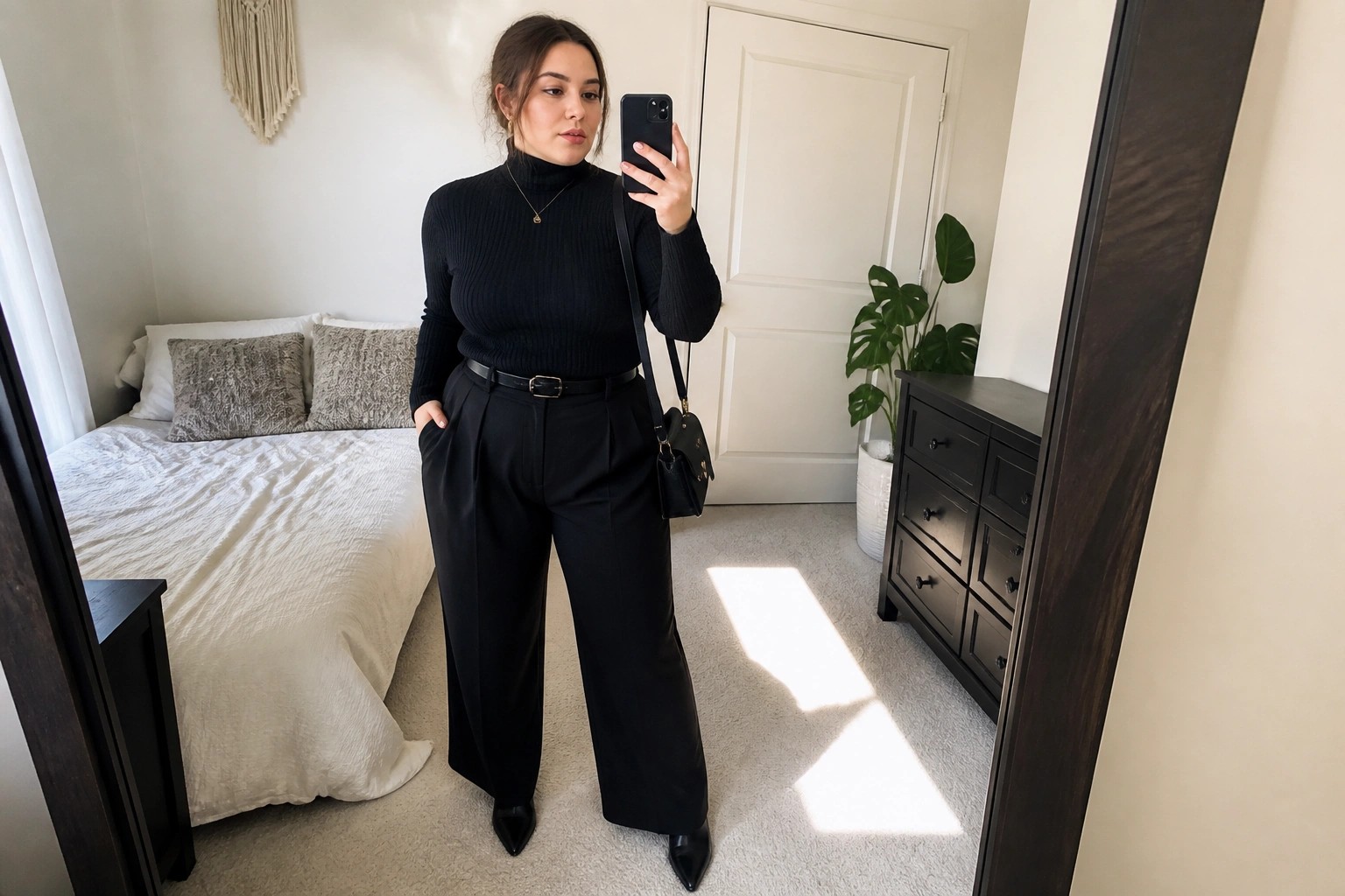 Woman taking mirror selfie in black turtleneck and wide-leg pants in bedroom
