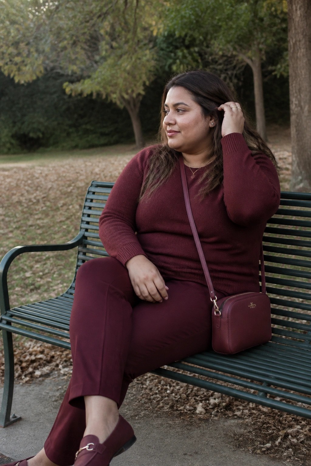 Woman in maroon sweater and pants on green park bench with matching bag