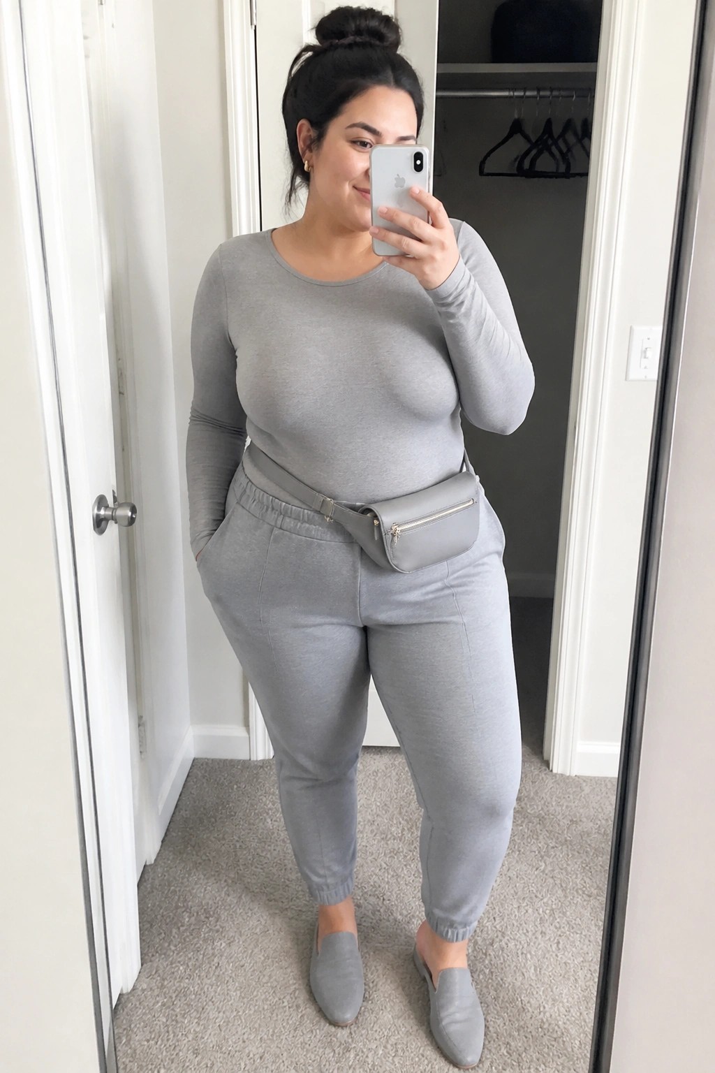 Woman in gray loungewear taking mirror selfie with belt bag and phone
