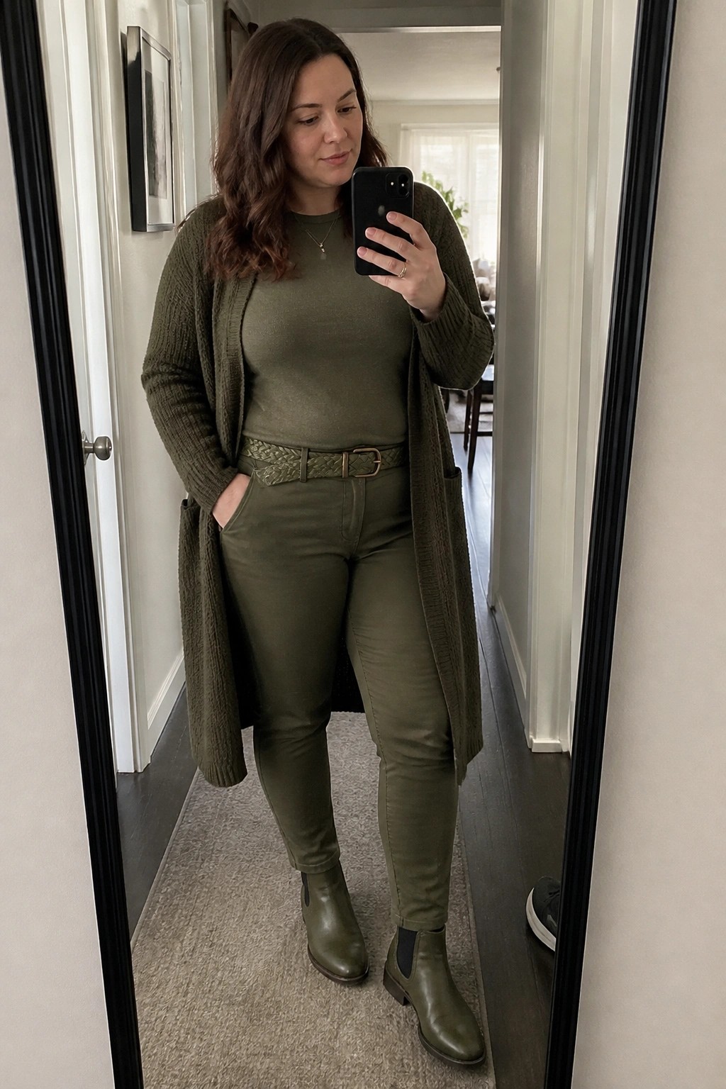 Woman wearing an olive green monochrome outfit with a long open knit cardigan over a fitted top and slim pants, completed by a braided belt and matching green ankle boots.