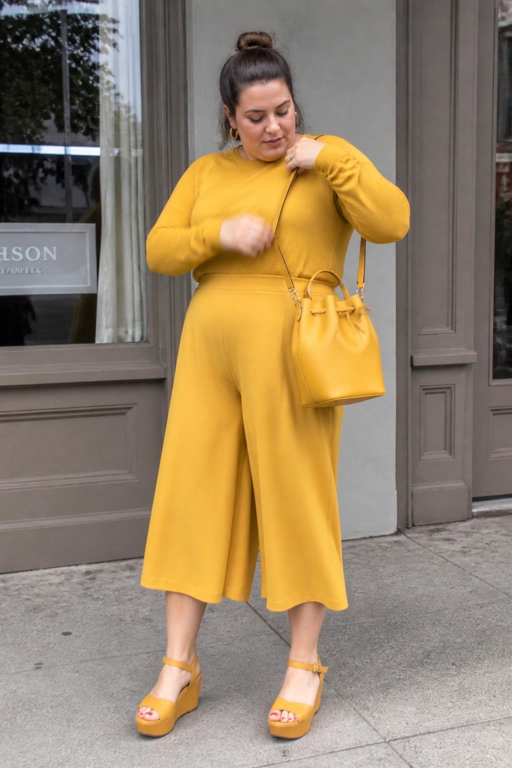 Woman in yellow sweater and culottes with matching bucket bag and wedges outdoors.