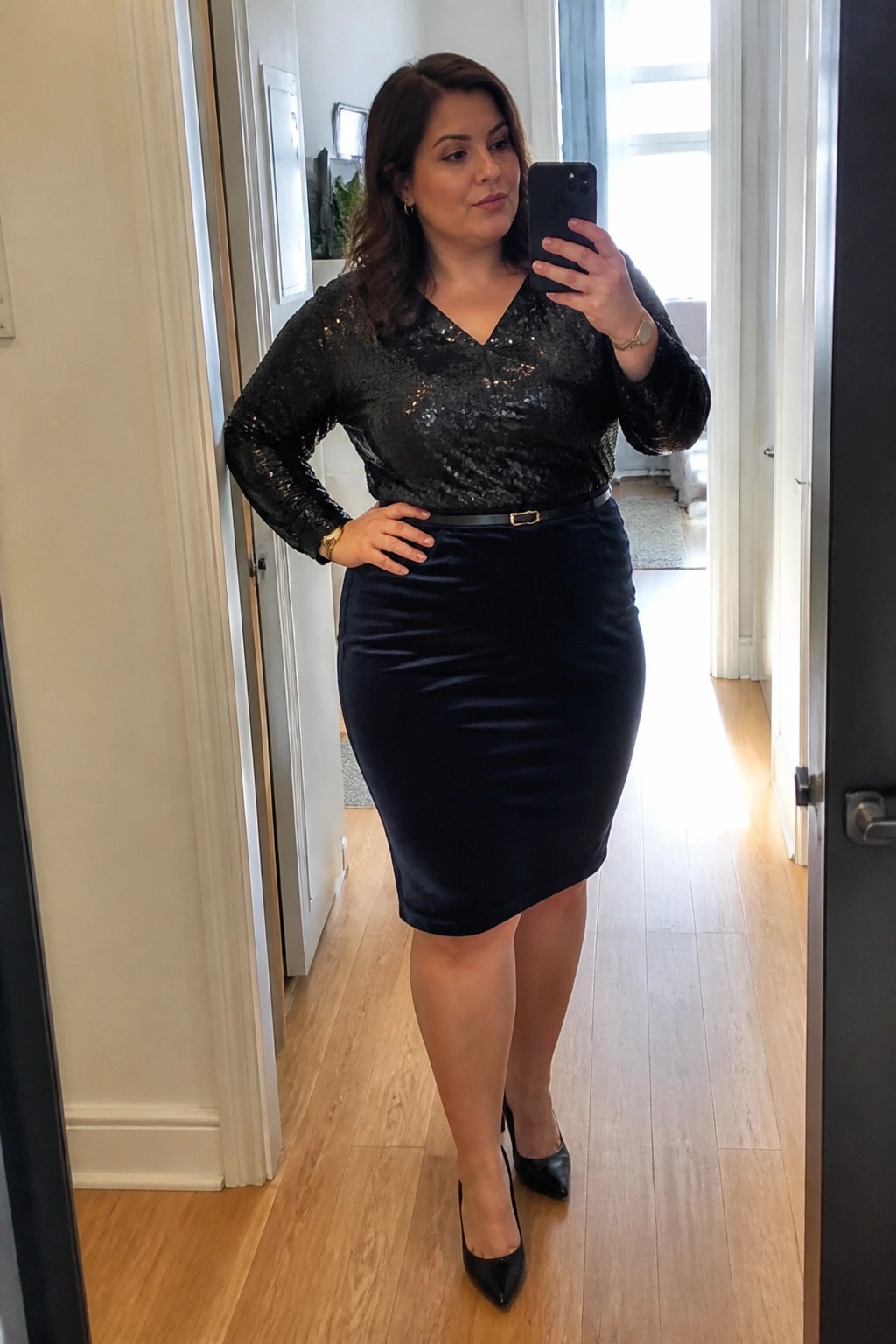 Woman in black sequined top and velvet skirt taking mirror selfie in hallway