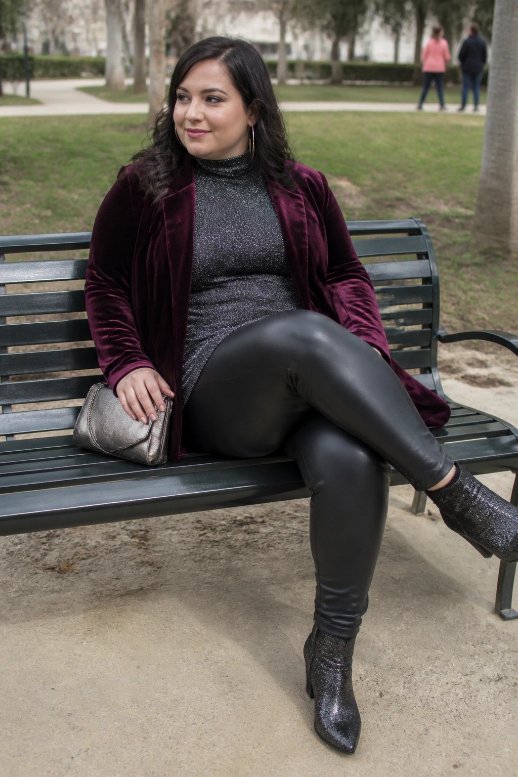 Woman in maroon velvet blazer and black leggings on park bench with clutch.