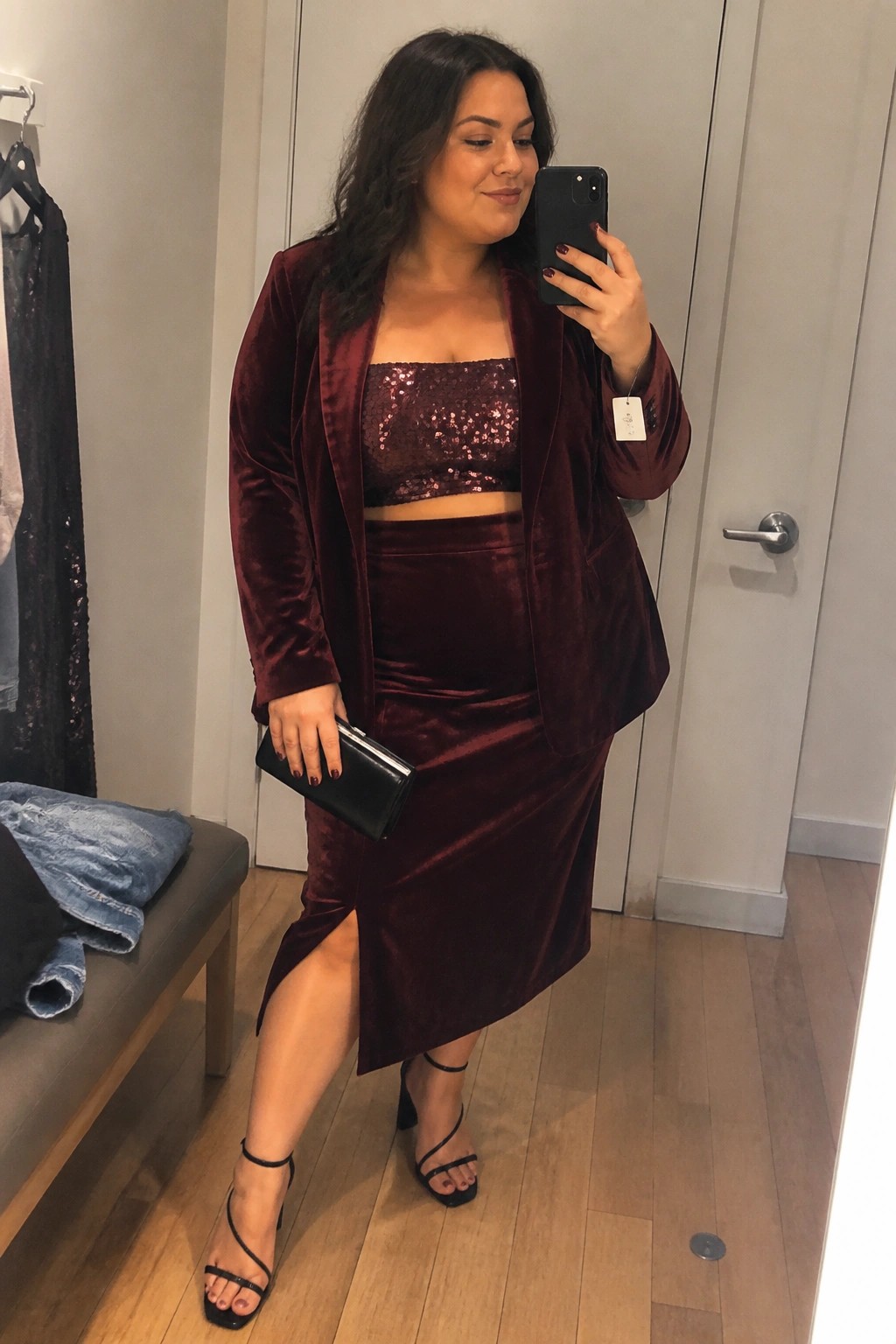 Woman in burgundy velvet blazer, sequin top, and skirt taking mirror selfie