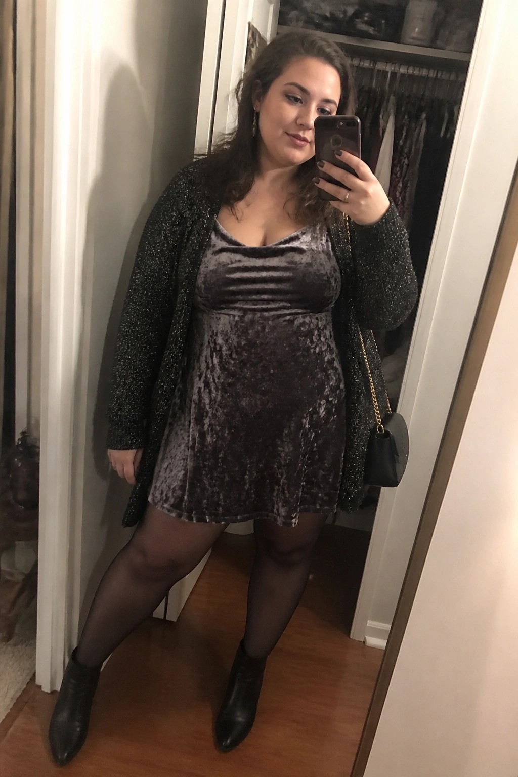 Woman in sparkly black cardigan over purple velvet dress taking mirror selfie