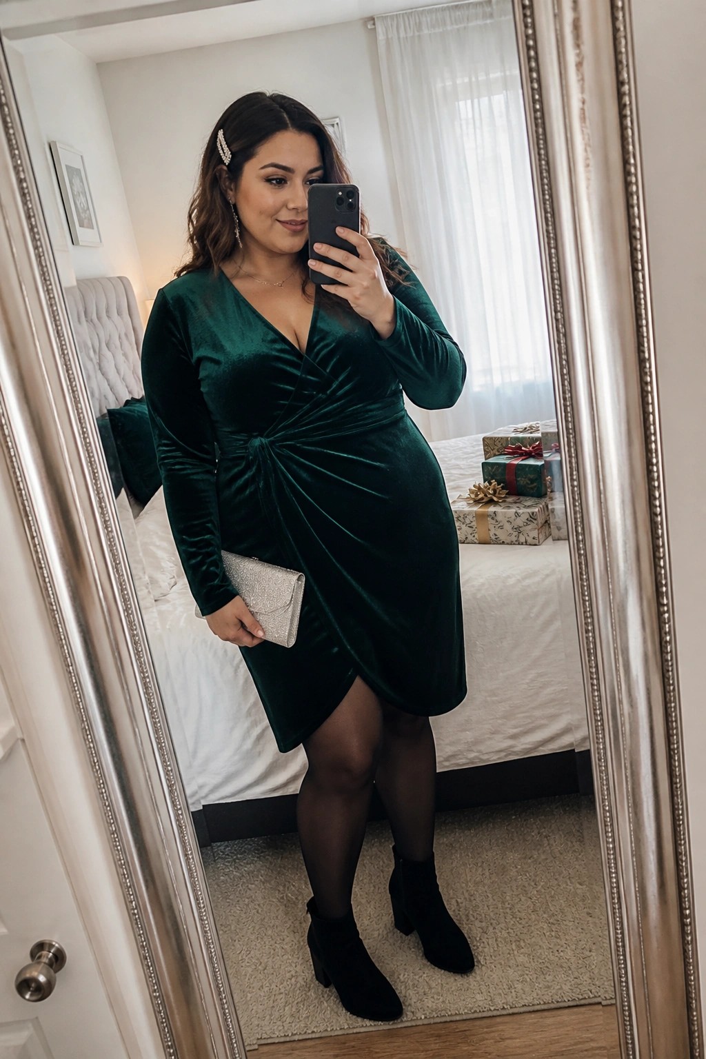 Woman in emerald green velvet dress taking mirror selfie in bedroom with gifts