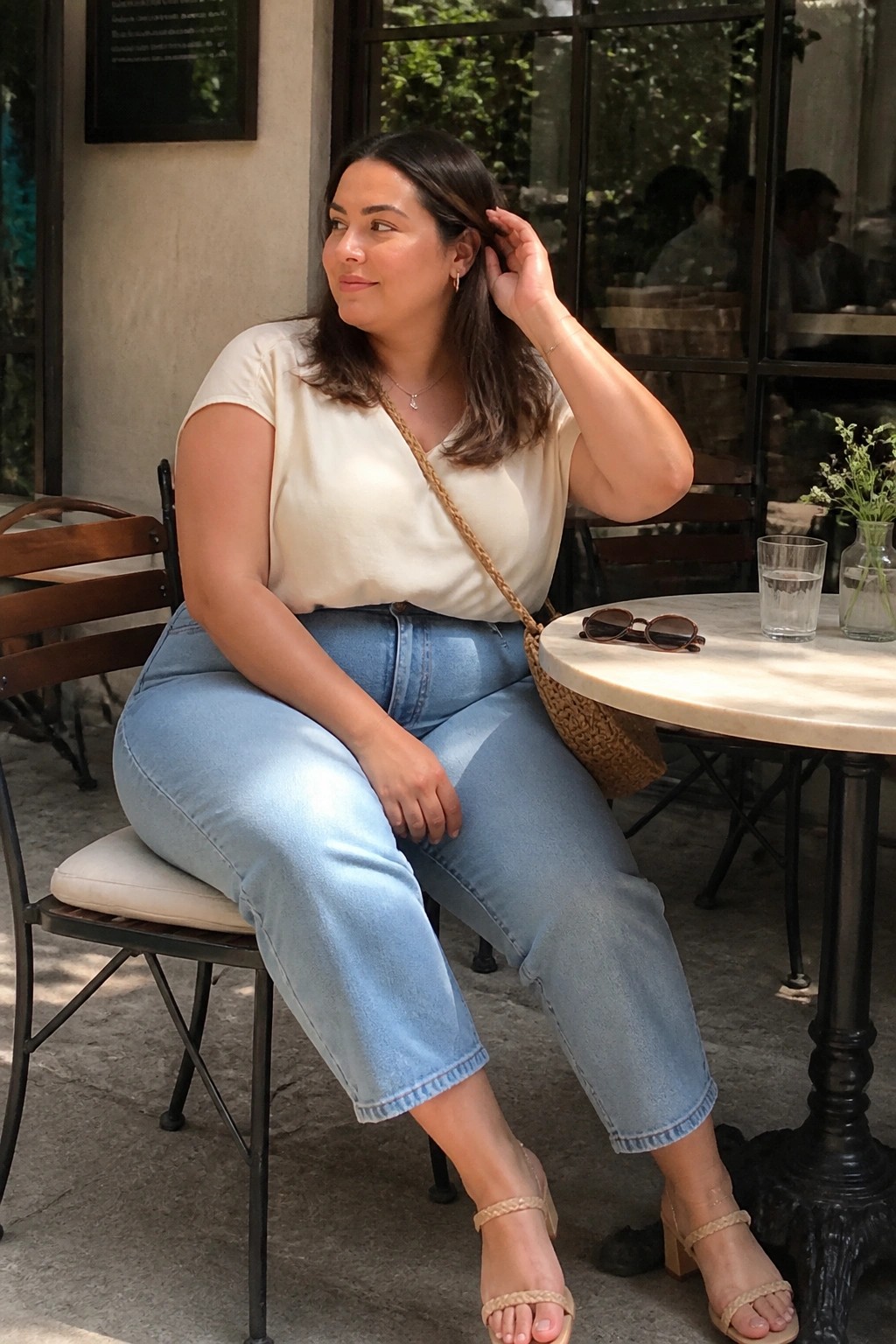 Woman in cream top and blue jeans seated at outdoor cafe table