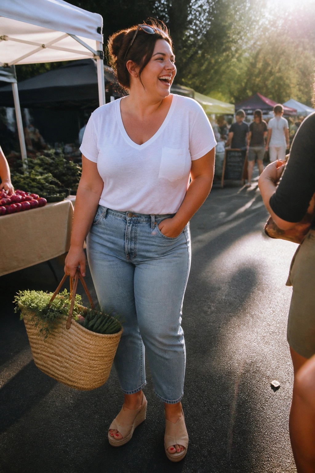 Plus size woman wearing a white v neck tee with a pocket and light wash straight leg jeans paired with beige wedge sandals while holding a woven basket at an outdoor market.