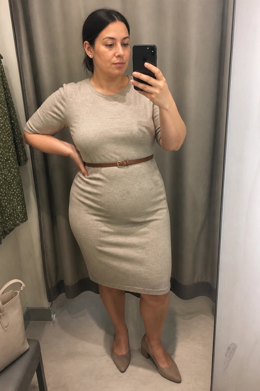 A plus size woman wearing a beige knit midi dress belted with a brown leather belt and taupe block heel shoes, posing in a mirror selfie for a professional outfit idea.