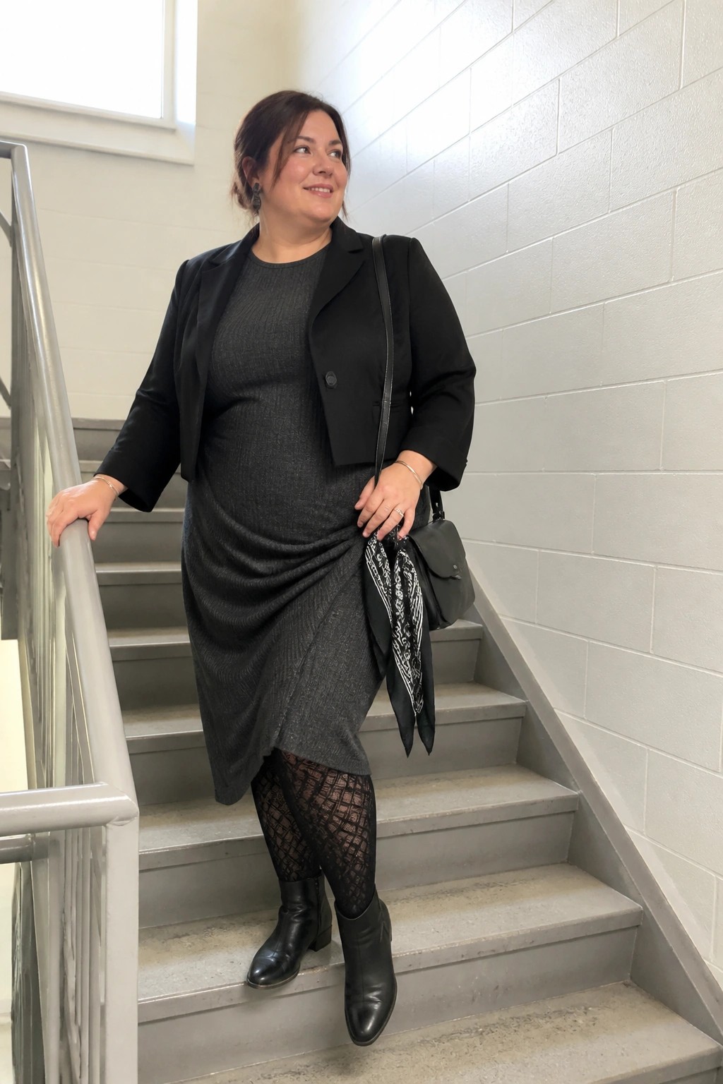 Woman in black blazer and gray dress on concrete stairs with handbag