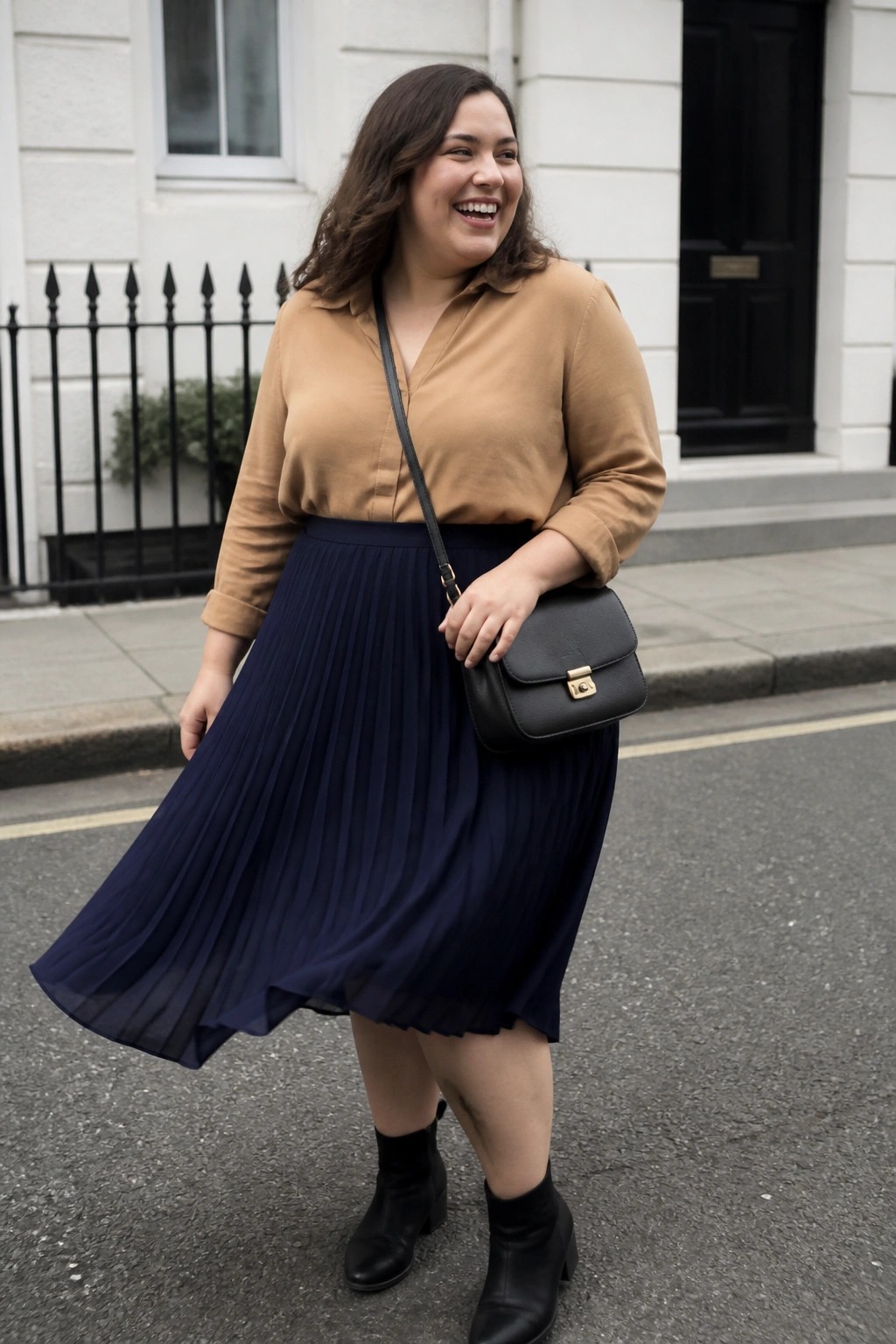 Smiling woman in tan blouse and navy pleated skirt with black bag on street