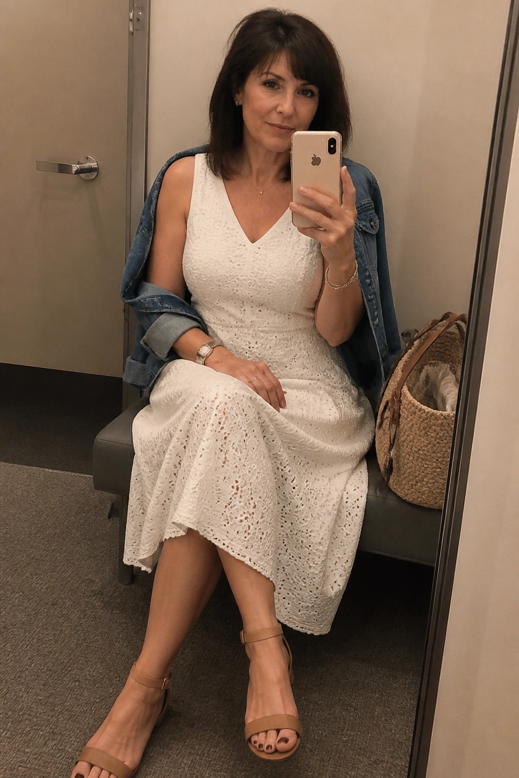 Woman in white lace dress and denim jacket taking mirror selfie with phone