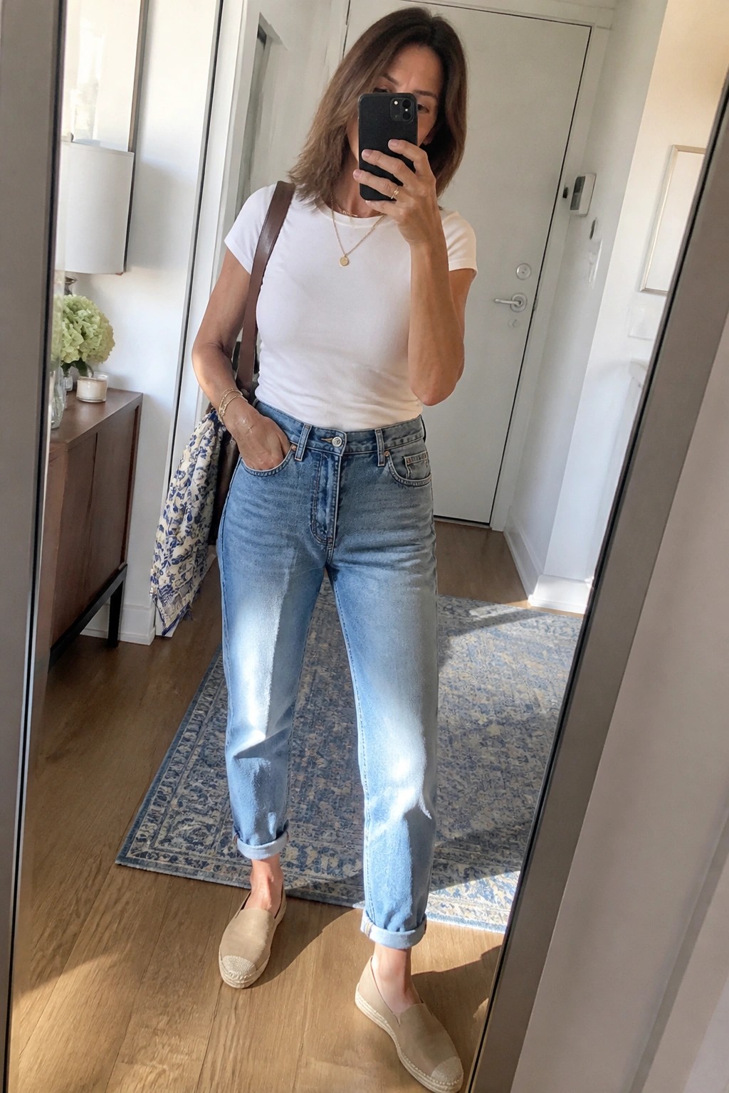 Woman in white tee and cuffed jeans taking mirror selfie in hallway