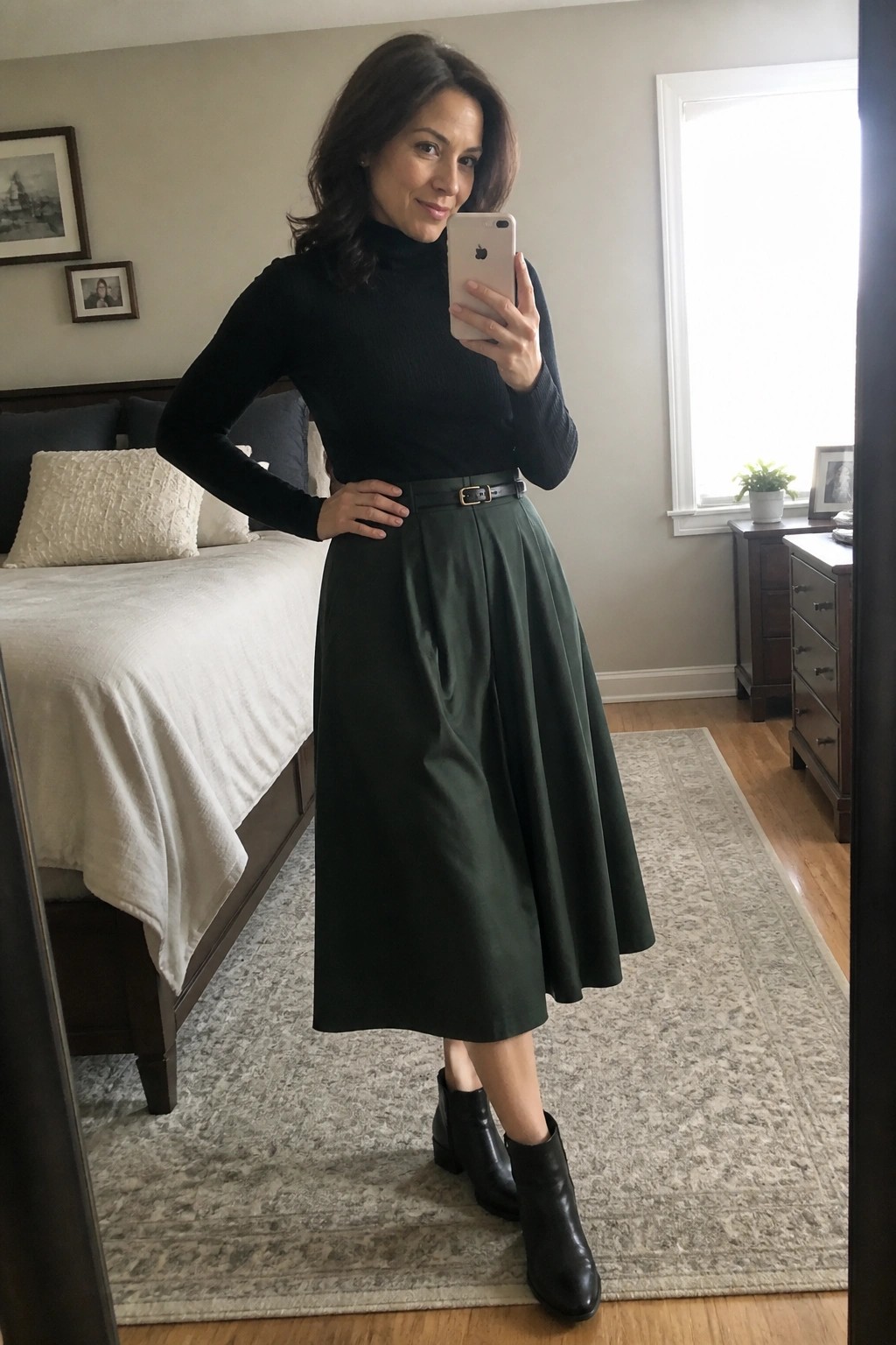 Woman in black turtleneck and green midi skirt taking bedroom mirror selfie