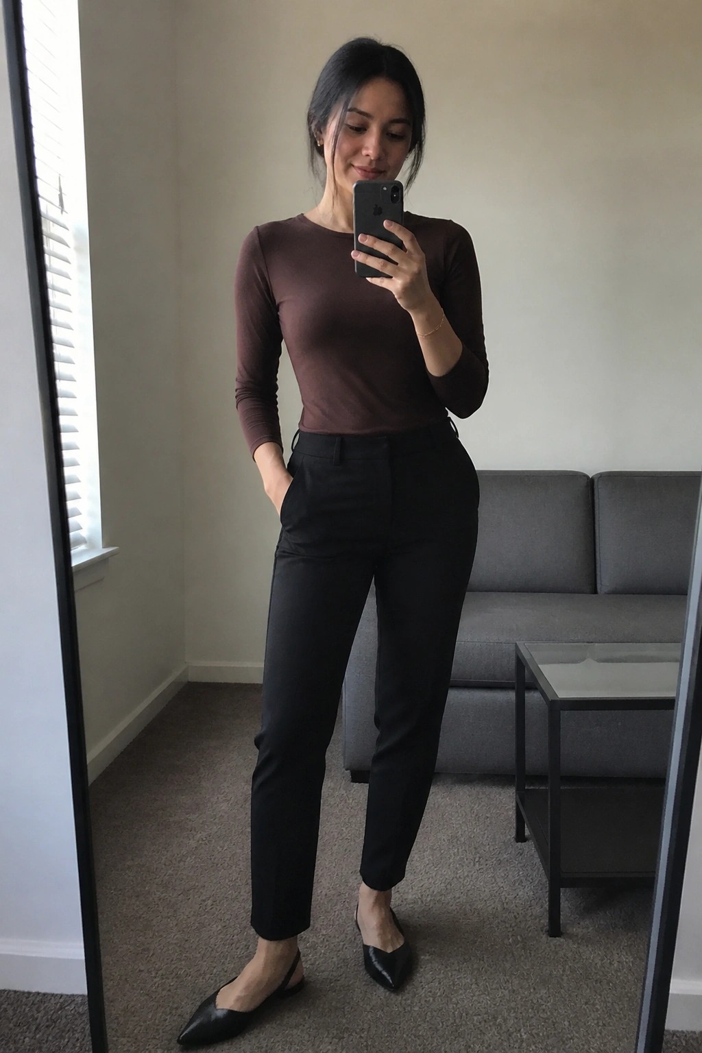 Woman in brown top and black pants taking mirror selfie with iPhone