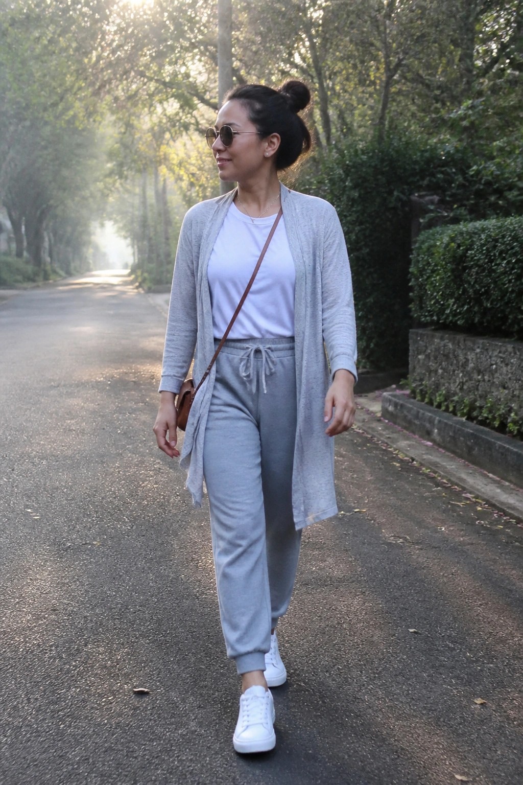 Woman in gray cardigan and sweatpants walking on sunlit tree-lined path
