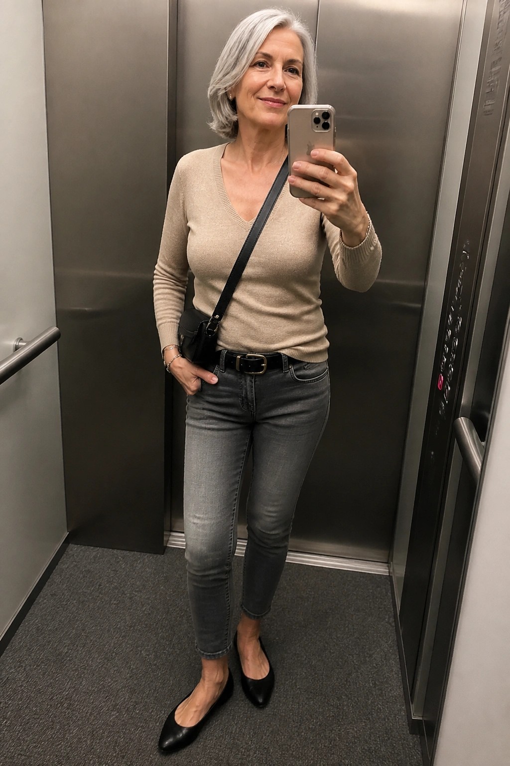 Woman with gray hair in beige sweater and jeans taking elevator selfie