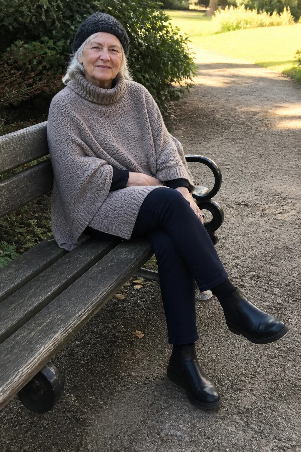 Elderly woman in gray knit poncho and hat seated on park bench