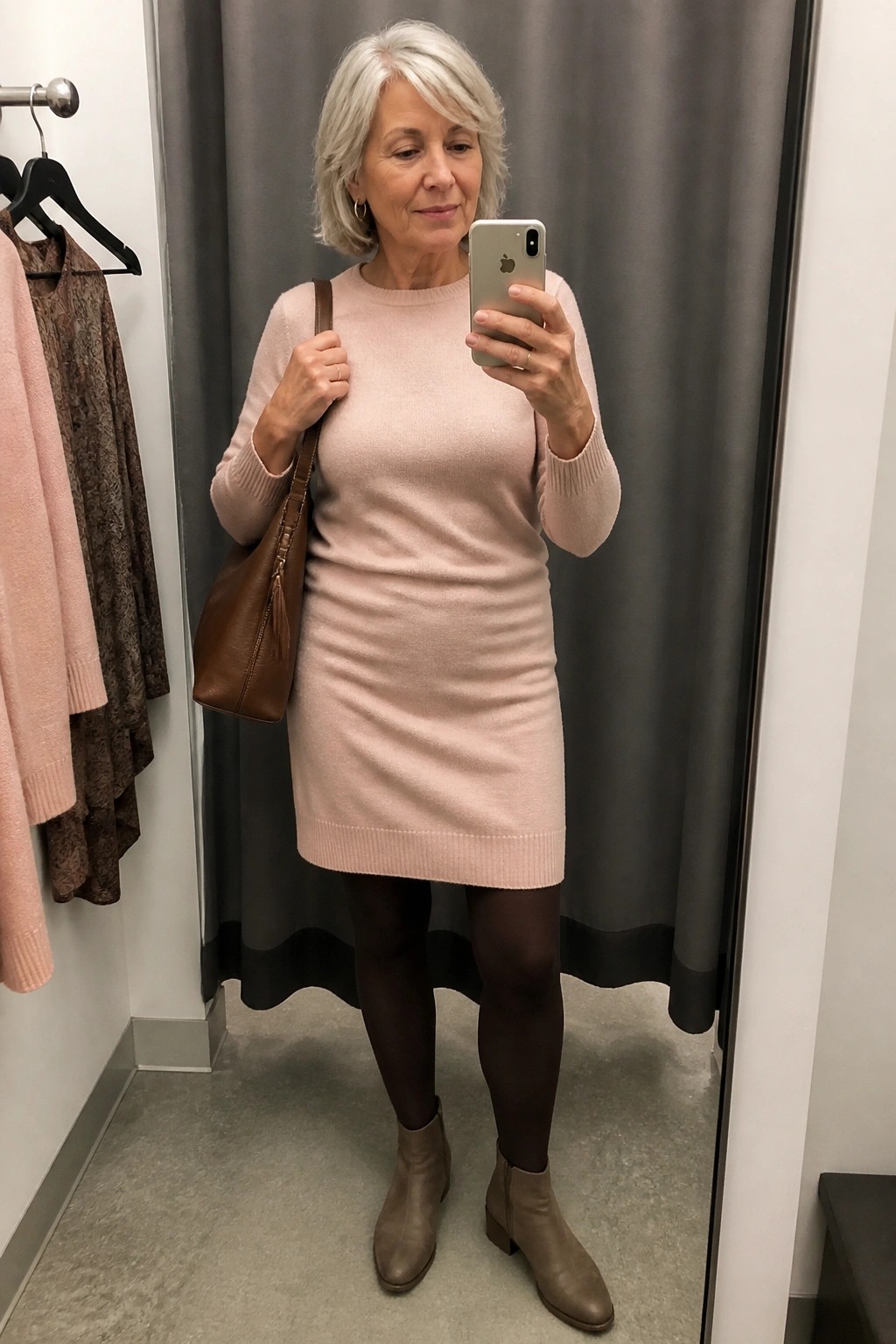 Gray-haired woman in pink knit dress taking mirror selfie in fitting room