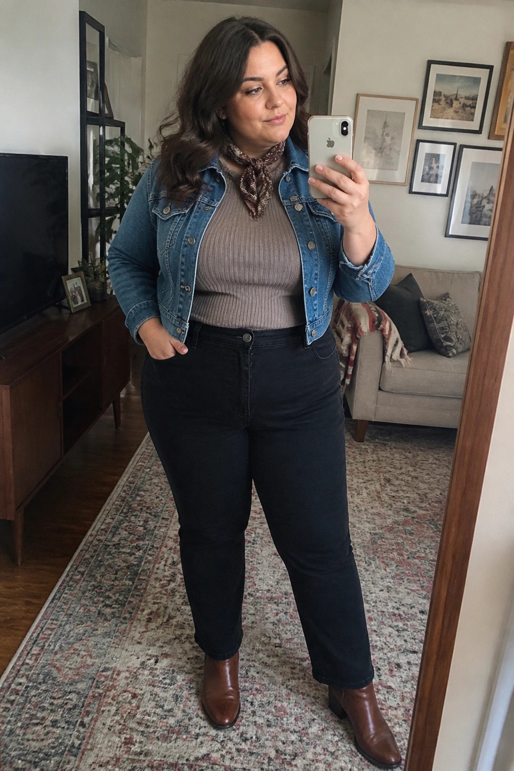 Woman in denim jacket and black jeans taking mirror selfie in living room