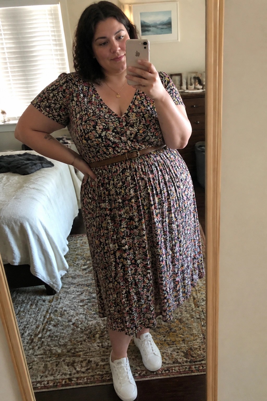 Woman in floral dress taking mirror selfie in bedroom wearing white sneakers