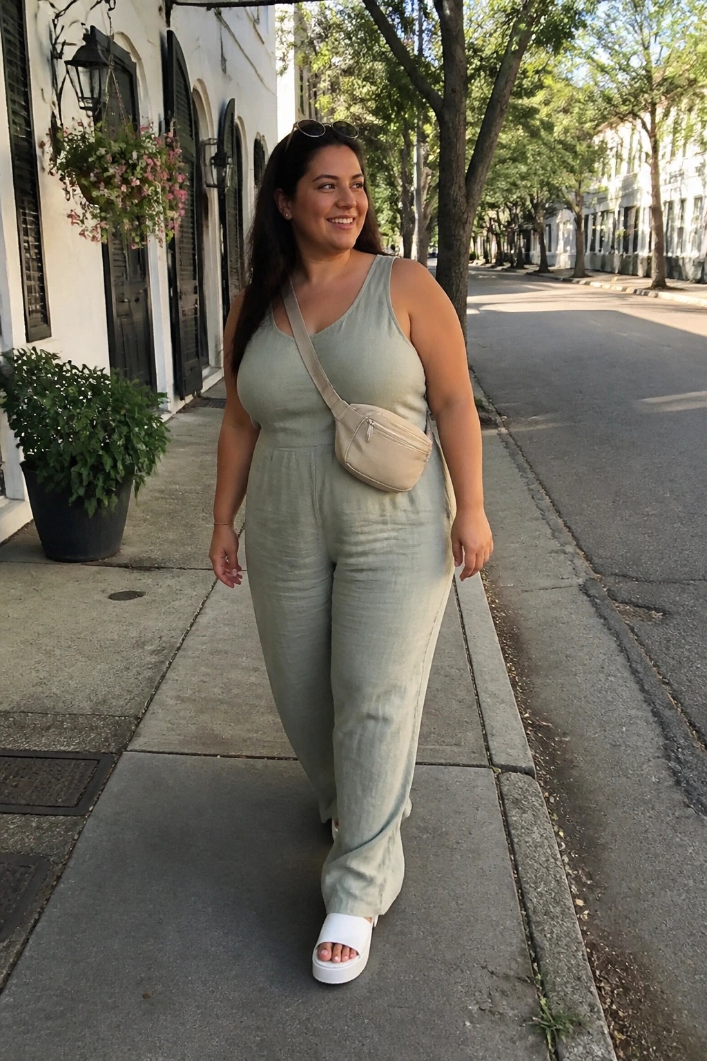 Smiling woman in sage green jumpsuit with beige crossbody bag on sidewalk