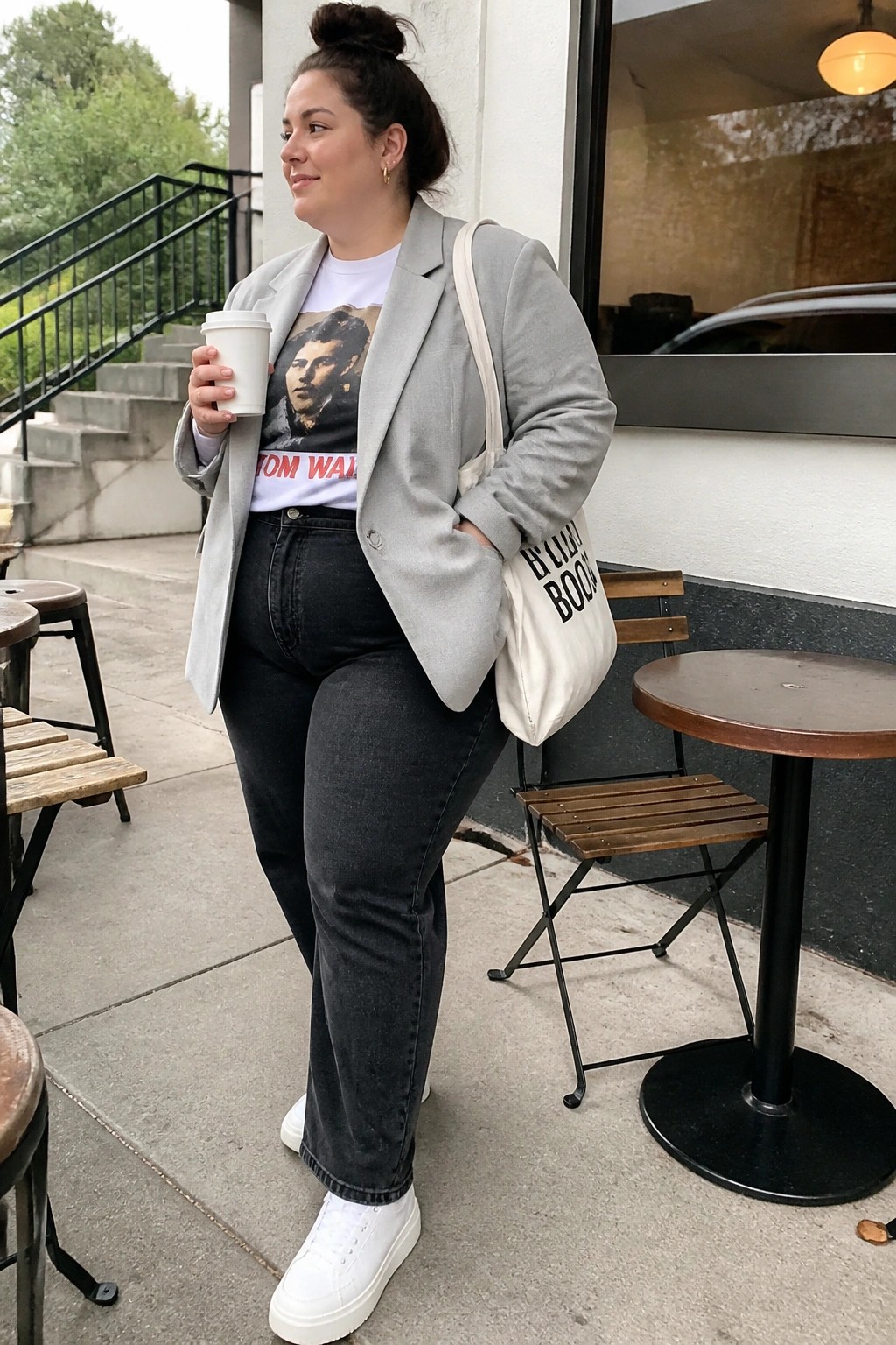 Woman in gray blazer holding coffee with tote bag at outdoor cafe