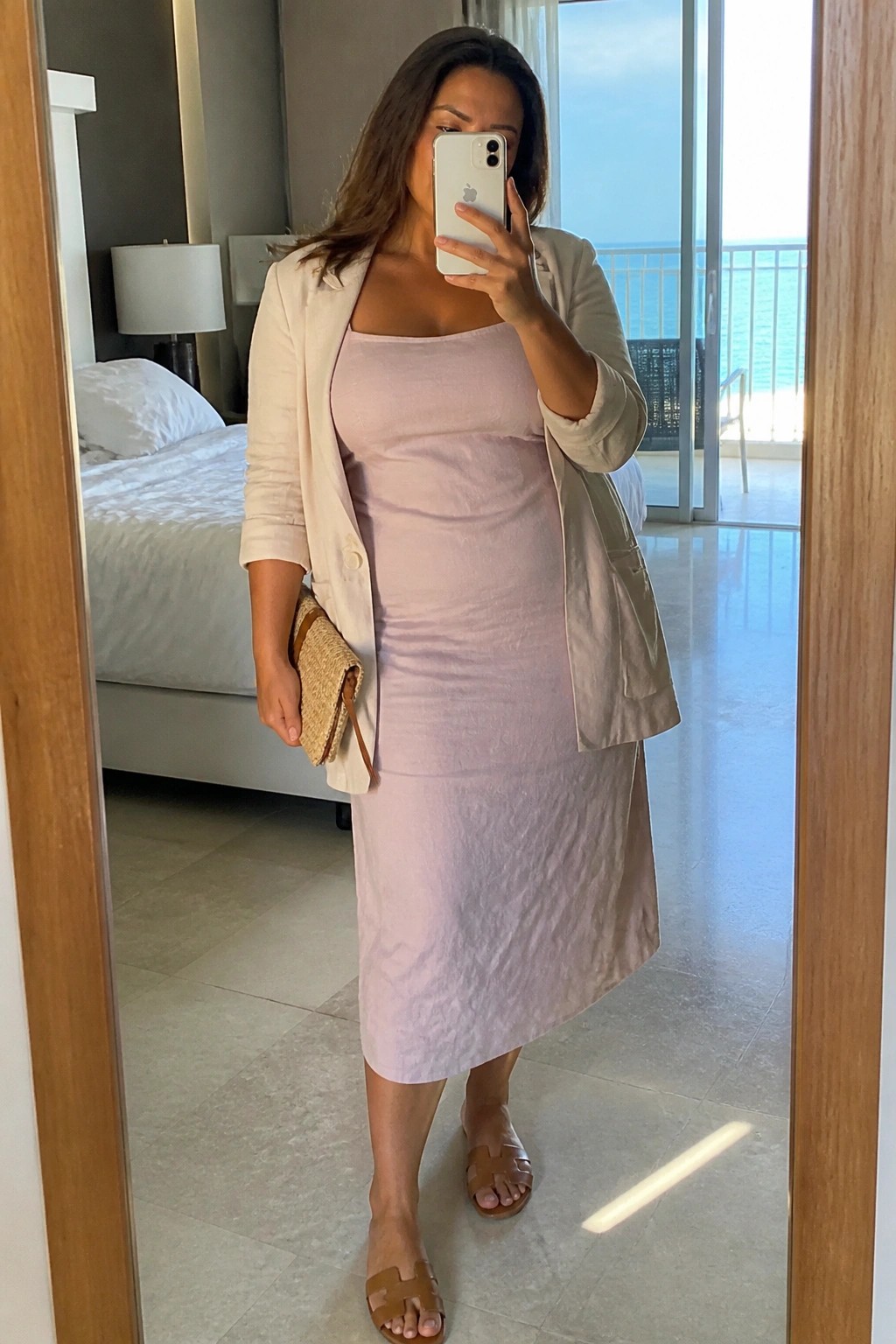 Woman in pink dress and beige blazer taking mirror selfie with ocean view