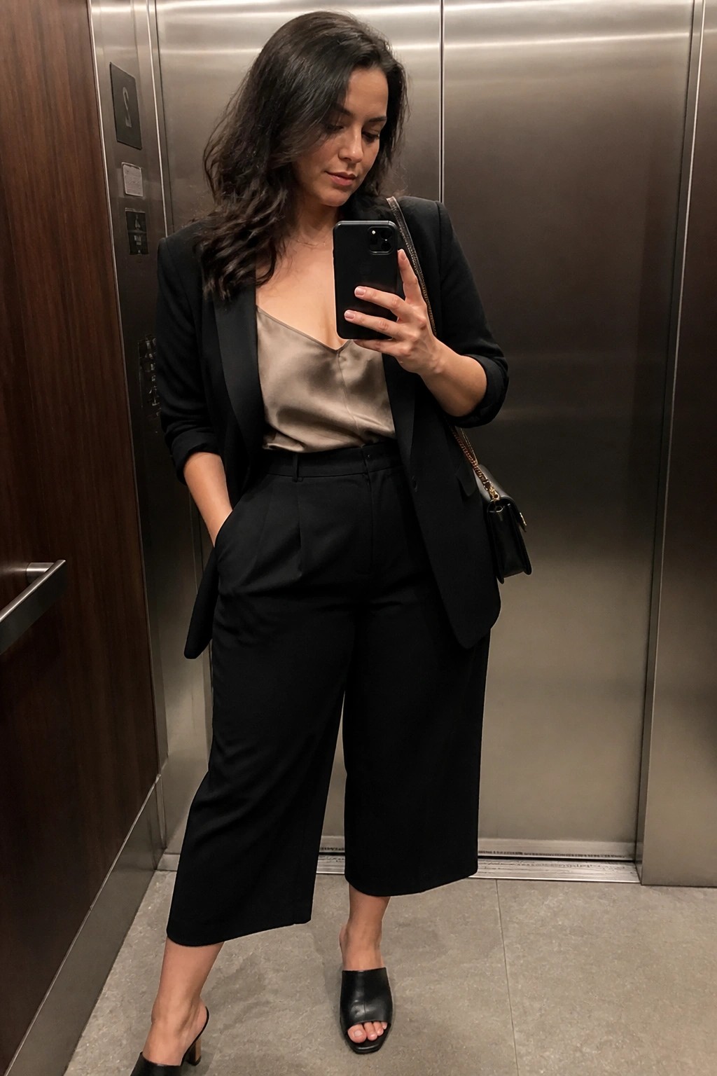 Woman in black blazer and satin top taking selfie in elevator
