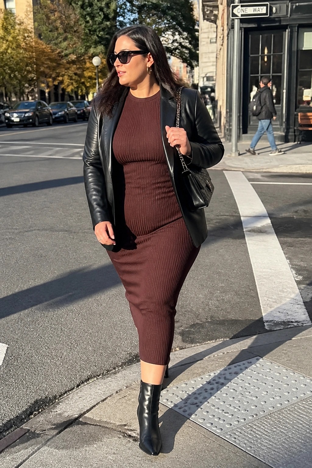Woman in brown ribbed dress and black leather jacket on city street