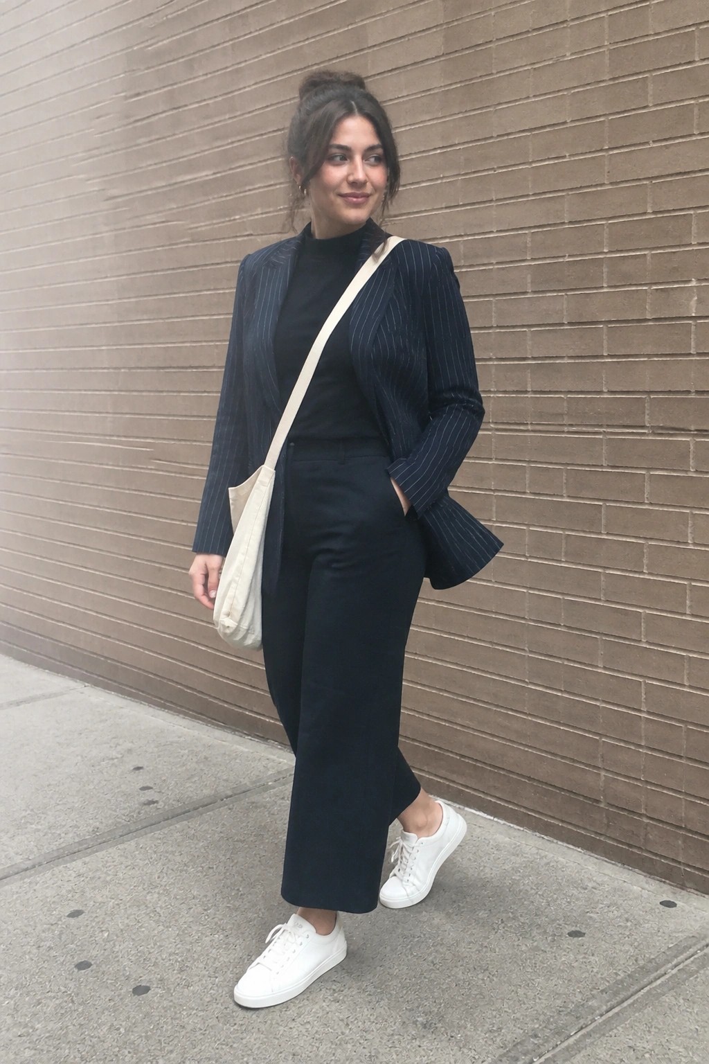 Woman in navy pinstripe blazer and trousers with white sneakers by brick wall