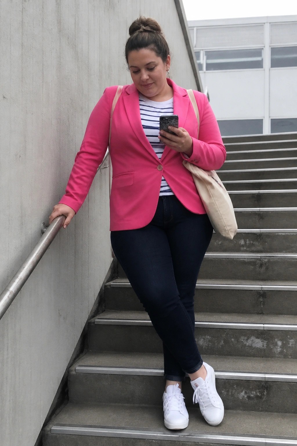 Woman in pink blazer checks phone on concrete stairs with tote bag