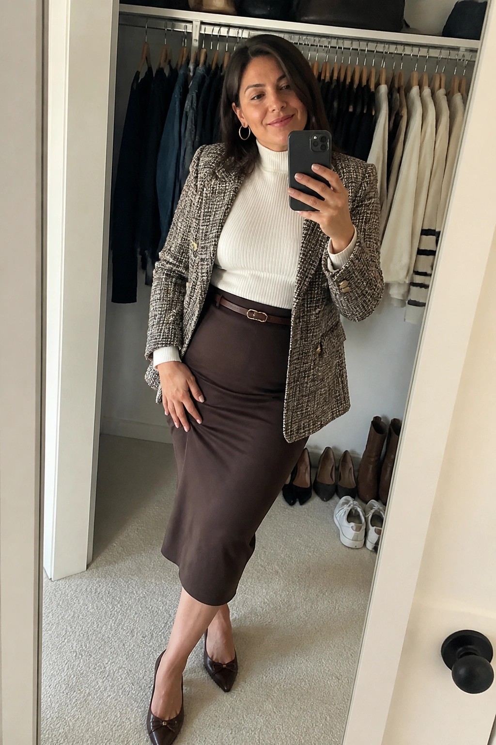 Woman in tweed blazer and brown midi skirt taking mirror selfie in closet