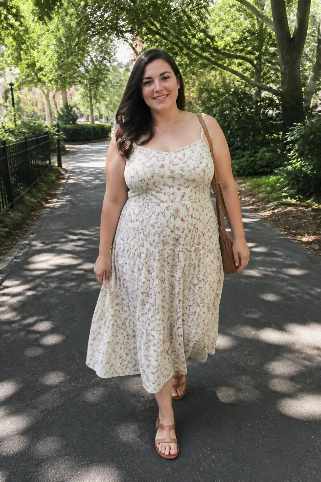 Smiling woman in white floral sundress carrying brown bag on sunny park path