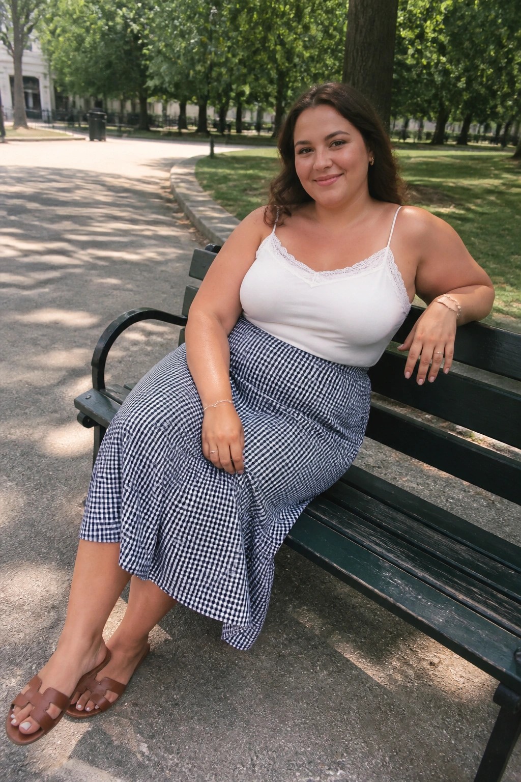 Woman in white camisole and blue gingham skirt on green park bench