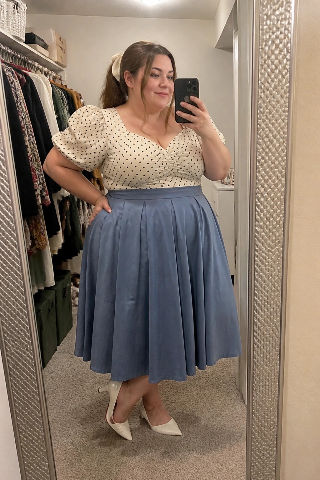 Woman in polka-dot top and blue pleated skirt taking closet mirror selfie