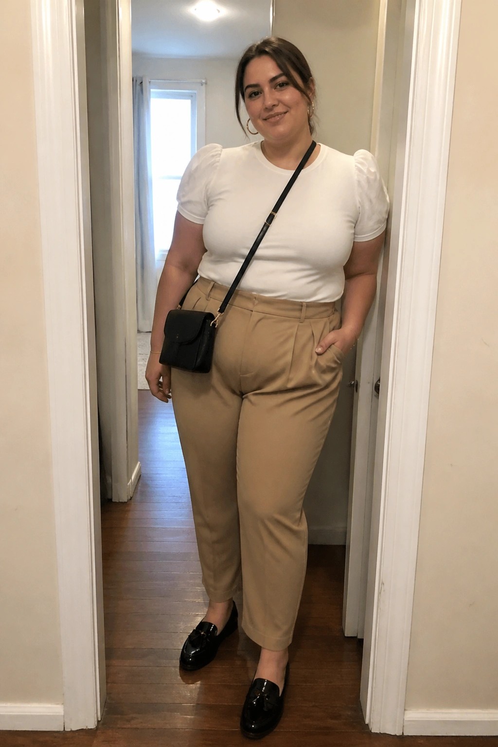 Woman in white puff-sleeve top, tan trousers, black crossbody bag in doorway